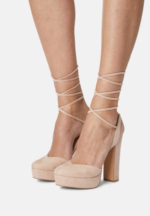 Scarpe con tacco alto in suede beige, dotate di un robusto plateau e cinturino alla caviglia. Texture liscia, design a punta e tacco a blocco alto.