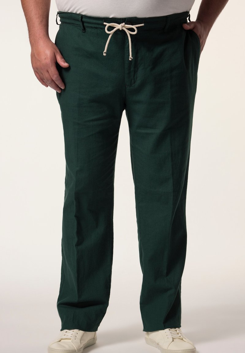 Pantaloni in lino verde con cintura elastica e cordino beige. Tasche visibili sui lati. Abbinati a sneakers bianche.