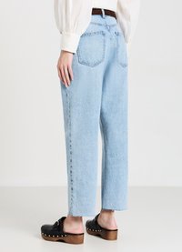 Jean bleu clair taille haute avec une coupe décontractée, jambe droite, ourlet effiloché et deux poches arrière, associés à des sabots noirs.