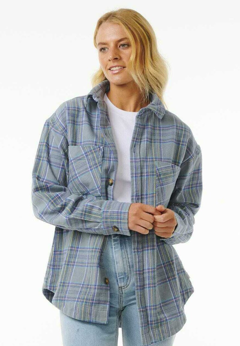 Camisa de cuadros abotonada en azul claro con líneas amarillas y verdes, de corte oversized, con dos bolsillos en el pecho y una textura de tela suave.