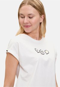 T-shirt en coton blanc à manches courtes retroussées, arborant trois motifs de fantômes pixelisés en noir et blanc avec un accent jaune.