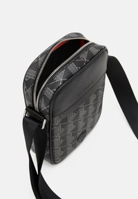 Black shoulder bag with geometric gray pattern, leather accents, silver zipper, and adjustable black strap. Red interior lining visible.