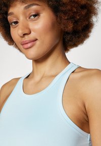Light blue athletic tank top with a smooth texture, racerback design, and soft stitching details. Close-up of neckline and shoulders.
