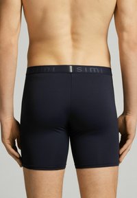 Mörkblå boxerkalsonger gjorda av stretchigt material. Har en åtsittande design med ett elastiskt midjeband märkt "SIMI." Ingen framträdande mönster.
