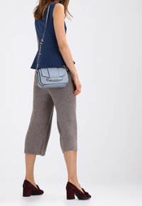 Ljusblå axelväska med en strukturerad design, silverdetaljer och en justerbar rem, parat med grå ribbade culotter och vinröda klackar.