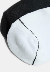 Detailní záběr na černobílé kotníkové ponožky ukazující švy a texturu látky na jednoduchém pozadí.