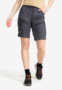 Grå cargoshorts med flera zip-fickor, justerbar midja och stickad söm. Kombinerat med mörka sneakers och kontrasterande snören.