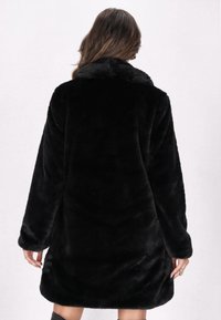 Cappotto in pelliccia sintetica nera con una consistenza morbida, maniche lunghe e colletto. Presenta una vestibilità comoda e arriva fino a metà coscia, con dettagli minimi.
