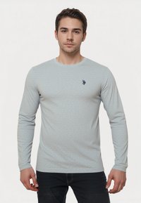 Világoskék, hosszú ujjú póló, texturált anyagból, kerek nyakkivágással, és egy kis sötétkék logóval a bal mellrészen.