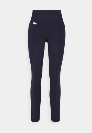 Leggings bleu marine taille haute avec des rayures texturées subtiles sur le bas des jambes et un petit logo blanc sur la hanche gauche supérieure.