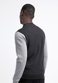 Černá a šedá mikina s texturovaným tělem, žebrovanými manžetami a kulatým výstřihem. Rukávy jsou šedé s hladkým povrchem.