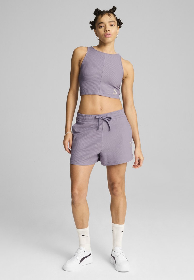 Paarse geribde crop top met een ronde halslijn en logo, gecombineerd met bijpassende shorts met trekkoord. Witte sportschoenen en sokken maken de look compleet.