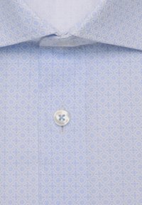 Chemise bleu clair avec un motif géométrique subtil et un bouton blanc fixé sous un col rabattu.