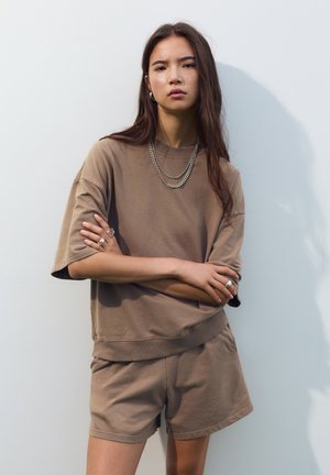 Brauner, oversized Baumwollpullover mit kurzen Ärmeln und passenden Shorts. Verfügt über einen gerippten Saum und geschichtete Silberketten.