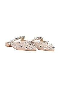Mules beige de punta afilada con tacón plano, adornadas con tachuelas esféricas plateadas a lo largo de la parte superior y un diseño de tiras cruzadas.
