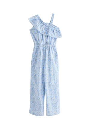 Ung kvinde iført lyseblå blomsterprintet jumpsuit med ét skulderstrop og flæsedetalje, stylet med hvide sneakers og et matchende armbånd.