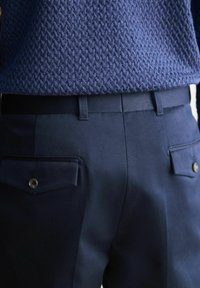 Mornarska hlače glatke teksture, sa dva stražnja džepa sa dugmadima i ravnim pojasom, u kombinaciji s teksturiranom mornarskom puloverom.