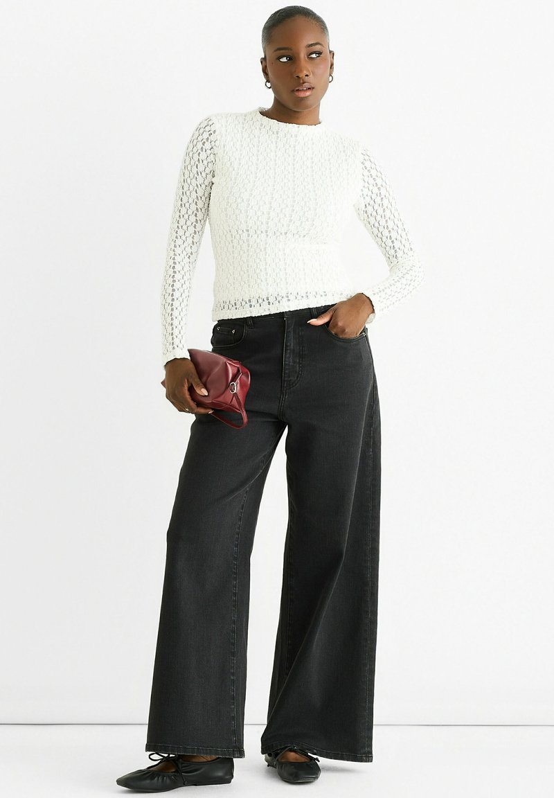 White knitted long-sleeve top with a textured pattern, paired with high-waisted black wide-leg jeans and a small maroon clutch.