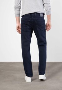 Jean bleu foncé à coupe droite, avec deux poches arrière et des coutures décoratives. Associé à des baskets blanches et un pull gris.