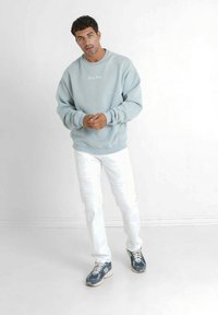 Felpa azzurra chiara con logo "Sixth June", jeans bianchi strappati e sneakers blu navy; vestibilità rilassata, texture morbida e design casual.