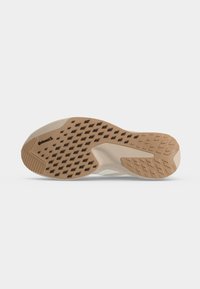 Semelle de chaussure beige et fauve avec des sculptures en forme de losange et des zones de grip texturées, présentée sur un fond clair uni.