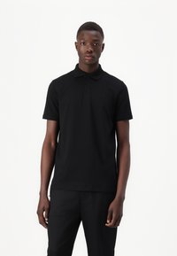 Black polo shirt made of smooth cotton. Features a classic collar, short sleeves, and three-button placket. Subtle logo on the chest.