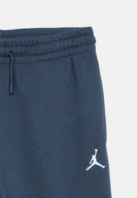 Σκούρες μπλε φόρμες από βαμβακερό ύφασμα, με ριμπ εφαρμογή στη μέση και λευκό λογότυπο Jordan στο κάτω αριστερό πόδι.