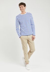 Stripet langærmet t-shirt i hvid og blå, parret med beige bukser og hvide sneakers. Har en rund halsudskæring og slim fit.
