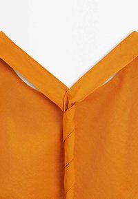 Gros plan d'une bretelle d'épaule en tissu orange reliée par un détail de couture torsadée sur un vêtement.