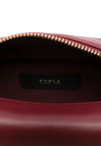 Interno di una borsa in pelle rosso intenso con cerniera dorata ed etichetta nera cucita all'interno con la scritta "FURLA Since 1927".
