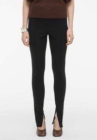 Sorte leggings med en tætsiddende design, der har sideslids ved kanten og diskret sømdetalje. Båret med brune hæle.