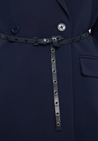 Ναυτικό σακάκι με αντίστοιχο μαύρο ζωνάκι με οπές και λεπτομέρεια κόμπου, κατασκευασμένο από ύφασμα με λεία υφή και κομψό σχέδιο.