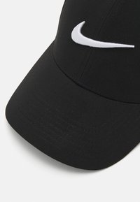 Sort baseball cap med en buet skygge, lavet af tekstureret stof, med et hvidt broderet Nike swoosh på forsiden.