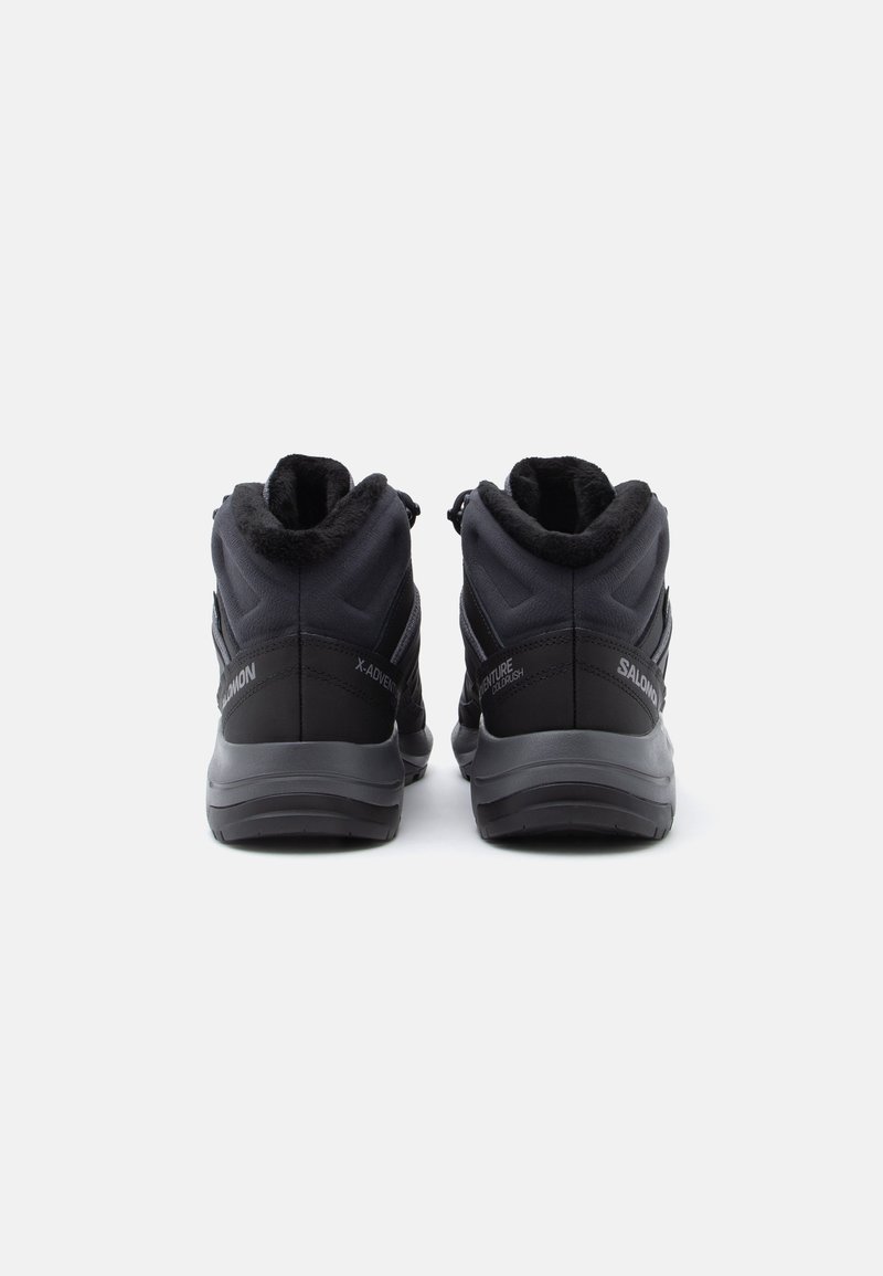 Scarpe da trekking nere con design a metà altezza, materiale testurizzato, fodera in morbido pellicciotto e suola grigia a contrasto. Branding visibile sui lati.