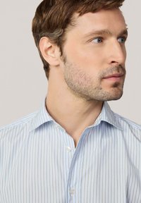 Camisa de rayas azul claro con cuello abotonado. La tela es suave, con finas rayas verticales en un tono más claro.