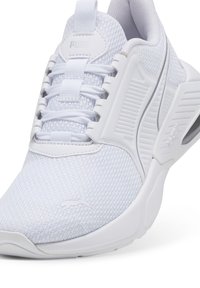 Weiße Sportschuh mit einem Obermaterial aus Mesh, gepolstertem Kragen, strukturierten Akzenten und einer Gummisohle mit sichtbarer Luftpolsterung. Logo sichtbar an der Seite.