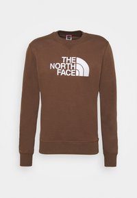 Sudadera marrón de tela suave, con cuello redondo y puños acanalados, que presenta un gran logo blanco impreso en el frente.