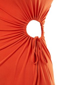 Oranje stof samengebracht in een ronde uitsnede met een gestrikte strik aan de rand, waardoor een geplooid detail op een kledingstuk ontstaat.