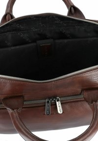 Bruine leren tas met een bovenrits, voorzien van gebogen handvatten, een gladde buitenkant en een zwart interieur met subtiele branding.