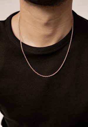 Dünne, roségoldene Halskette mit geflochtenem Design, die auf einem texturierten schwarzen Rundhalsausschnitt-Shirt liegt. Fokus auf dem subtilen Glanz der Kette.