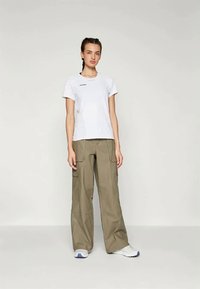 Biele bavlnené tričko s krátkymi rukávmi a malým čiernym logom, skombinované s voľnými khaki cargo nohavicami so bočnými vreckami.