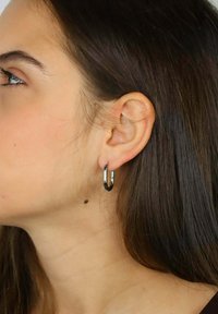 Srebrne kolczyki-koła, małe i błyszczące, o gładkim, zaokrąglonym kształcie. Zbliżenie pokazujące kolczyk noszony w uchu.