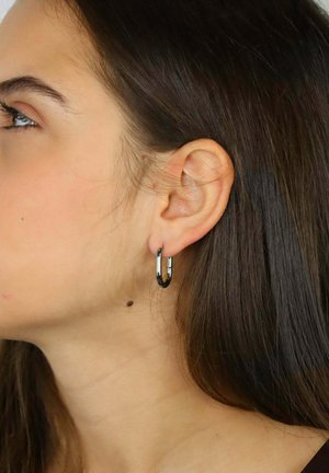 Orecchini a cerchio in argento, piccoli e lucenti, con un design liscio e arrotondato. Vista ravvicinata che mostra l'orecchino indossato all'orecchio.