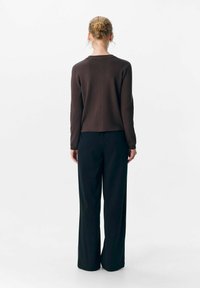 Brauner Strickpullover mit rundem Halsausschnitt, kombiniert mit hochtaillierten, schwarzen weiten Hosen. Glatte Textur, minimalistische Gestaltung.