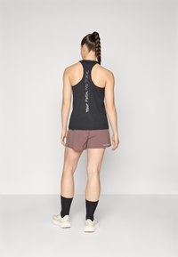Black racerback tank top with white text, paired with brown shorts and black socks. The outfit features a relaxed fit and soft fabric.