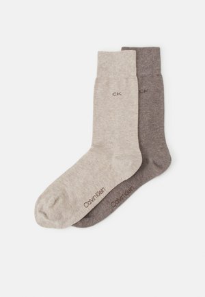 Deux paires de chaussettes Calvin Klein en gris clair et gris foncé, fabriquées en matériau doux et extensible, avec un logo près du bord.