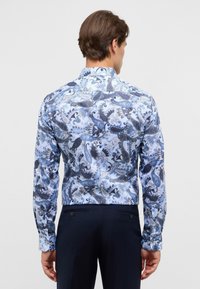 Camicia a maniche lunghe con bottoni di colore azzurro chiaro, decorata con un motivo paisley in blu navy e argento. Presenta un colletto classico e un tessuto testurizzato.