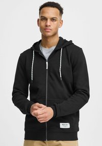 Sweat à capuche noir zippé en tissu doux avec un t-shirt intérieur gris. Comprend des cordons blancs et un patch logo sur l'ourlet. Coupe standard.