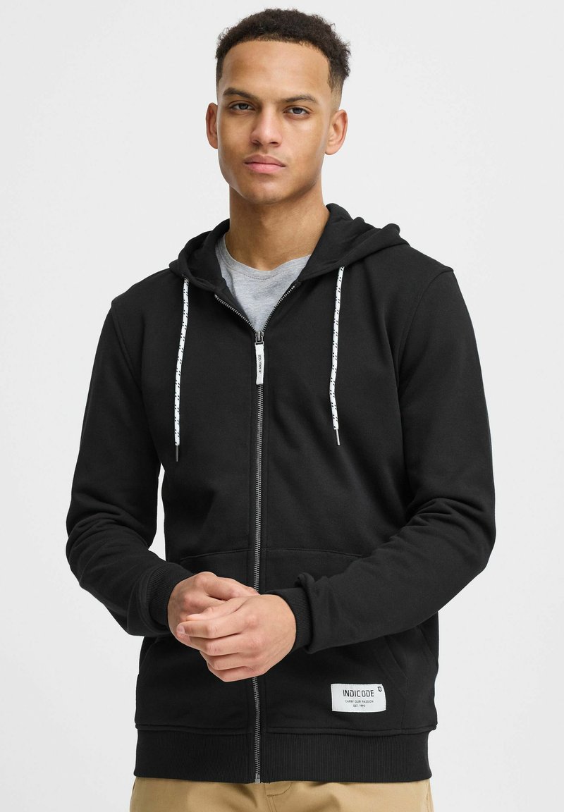 Sweat à capuche noir zippé en tissu doux avec un t-shirt intérieur gris. Comprend des cordons blancs et un patch logo sur l'ourlet. Coupe standard.