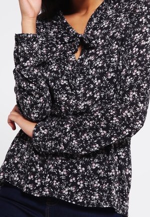 Schwarze Bluse mit langen Ärmeln, Schleifenkragen und leichtem Stoff. Verziert mit kleinen rosa und weißen Blumenmustern.